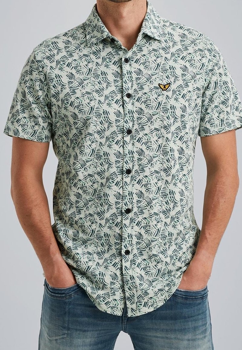 Camisa de manga corta con botones en verde claro, con un estampado de hojas en negro y verde oscuro. Incluye un pequeño logo bordado y botones negros.