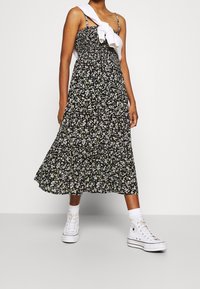 Květinové černé midi šaty s nařaseným živůtkem a tenkými ramínky, doplněné bílými vysokými teniskami a bílými kotníkovými ponožkami.