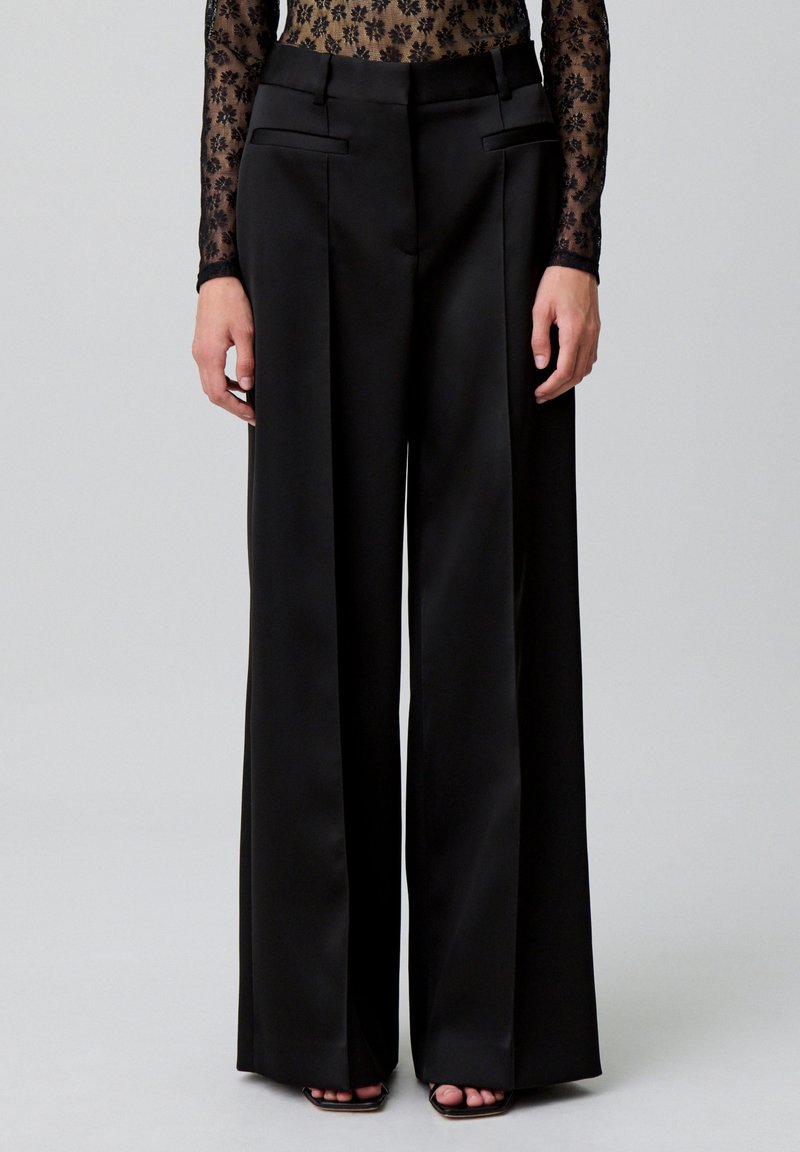 Pantaloni neri a gamba larga realizzati in un tessuto morbido con una vestibilità su misura, dotati di tasche laterali e vita alta. Design a fronte piatto per una maggiore struttura.