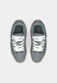 Des baskets grises en daim et en mesh, dotées de lacets blancs, d'un col rembourré et de légères variations de texture sur les côtés. Accents rouges à l'intérieur.
