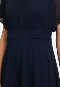 Robe bleu marine avec un corsage plissé et des manches courtes amples. Présente une taille bien définie et une jupe fluide avec une texture subtile.