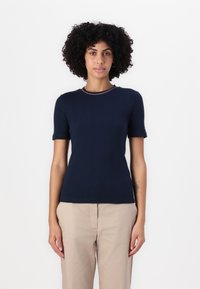 Top scurt cu mânecă în dungi de culoare bleumarin, cu guler rotund și detalii de contrast. Țesătura pare netedă și ajustată, asortată cu pantaloni bej.