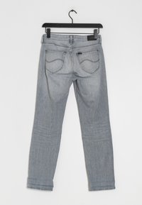 Jeans de mezclilla gris con un diseño de pierna recta, que cuentan con dos bolsillos traseros, detalles de costura sutiles y un bucle para colgar en un gancho negro.