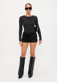 Μαύρο κορμάκι με μακριά μανίκια συνδυασμένο με λαμπερά μαύρα σορτσάκια από παγιέτα, μαύρες δερμάτινες μπότες ως το γόνατο και υπερμεγέθη μαύρα γυαλιά ηλίου.