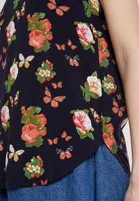 Kukka-aiheinen paita, jossa on tumma laivastonsininen tausta, jota koristavat värikkäät ruusut ja perhoset. Kevyt kangas, jossa on pyöristetty helma ja sivusplitit.