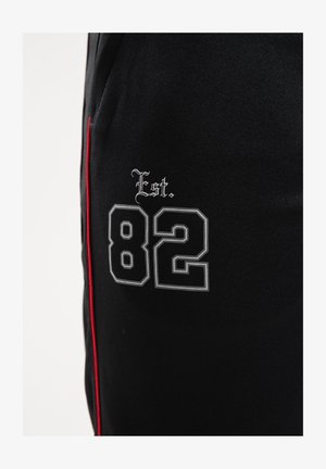 Black fabric featuring a white and grey embroidered "82" with "Est." above, accented with a red side stripe.