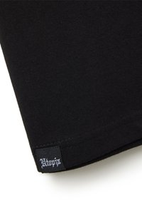 Cappio di t-shirt nera in cotone con un'etichetta cucita che presenta testo bianco. Texture liscia e design semplice senza motivi o accenti.