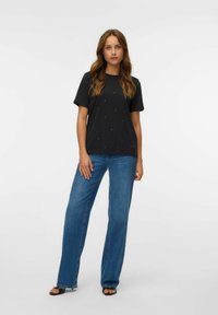 T-shirt nera a maniche corte, con decorazioni sparse. Abbinata a jeans a gamba larga blu chiaro e sandali neri.