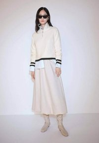 Cream knit pullover with black and white striped cuffs layered over a light blue shirt, paired with a flowy white skirt and beige boots.