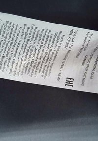 Etiqueta con instrucciones de cuidado y detalles de fabricación. El fondo es oscuro y la etiqueta es principalmente blanca con texto negro en varios idiomas.