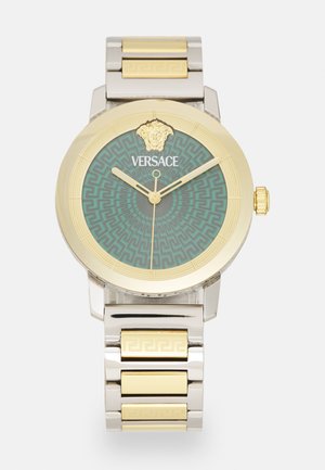 Relógio Versace com uma bracelete de metal prata e dourada, caixa redonda em tom dourado, mostrador com padrão verde, detalhes em dourado e um detalhe de cabeça de leão.