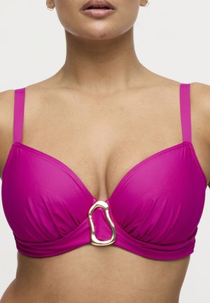 Vrouw draagt een felroze bikinitop met dunne bandjes en een decoratieve goudkleurige abstracte gesp in het midden vooraan.