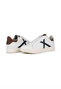 Sneaker in pelle bianca con design a croce blu navy, dettagli in suede marrone sul tallone e lacci piatti; suola in gomma testurizzata, stile pulito e minimalista.