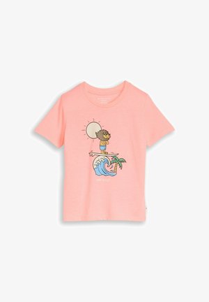 T-shirt rose avec un lion en dessin animé surfant sur une vague près d'un palmier sous un soleil éclatant.