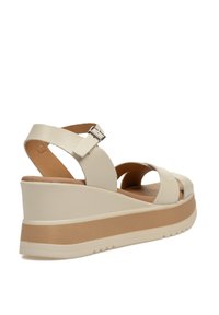 Sandalia de cuña en suave cuero blanco roto con tiras entrelazadas, hebilla ajustable en el tobillo y plantilla acolchada; suela de goma.