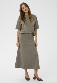 Divdaļīgs apģērbs, kurā ietilpst brīva stila pelēka blūze un saskaņota garā svārka, abi izgatavoti no mīksta auduma, apvienoti ar brūnām bloku papēžiem.