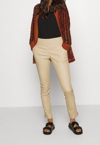 Beige tapered bukser med elastisk talje, matchet med en sort top og en strikket orange-rød cardigan. Sorte sandaler med spænde detaljer.