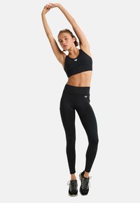 Zwarte sportbeha en high-waisted legging, gemaakt van een gestructureerde stof. Accessoires omvatten zwarte sportschoenen met grijze accenten.