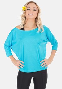 Turquoise loose-fitting top with 3/4 sleeves, round neckline, and soft texture, paired with black fitted leggings.