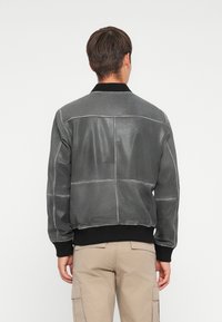 Chaqueta bomber de cuero gris con paneles cosidos, cuello y puños acanalados en negro, y una textura suave. Presenta un corte relajado.
