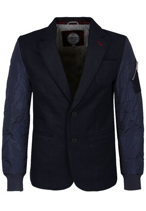 Blazer bleu marine foncé avec manches matelassées bleu marine, deux boutons sur le devant, poche zippée sur la manche gauche et détail de couture rouge sur le revers.