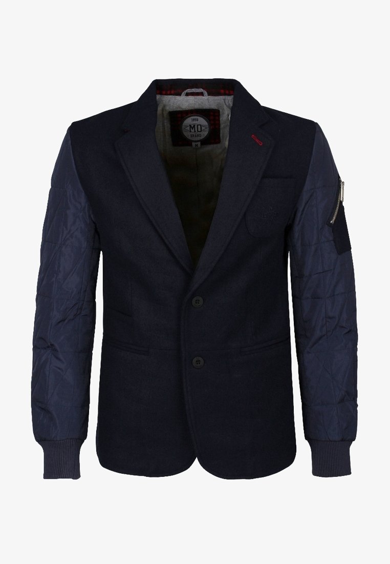 Blazer bleu marine foncé avec manches matelassées bleu marine, deux boutons sur le devant, poche zippée sur la manche gauche et détail de couture rouge sur le revers.