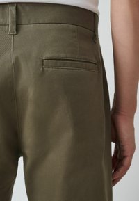 Pantalones verdes oliva con una textura suave, que presentan un bolsillo en la parte trasera y un corte ajustado, vistos de lado, destacando la pretina.