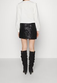 Blouse blanche à manches longues avec épaules bouffantes, associée à une mini-jupe noire pailletée et des bottes noires à genoux confortables avec des embellissements.
