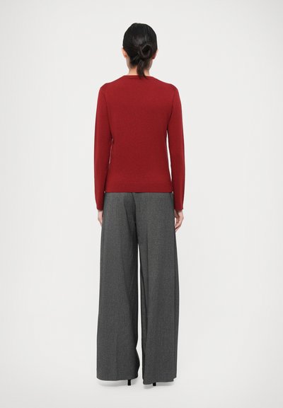 Red long-sleeve top with a round neckline, paired with wide-leg gray trousers featuring a textured pattern and subtle pleats.