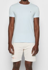 Helles blaues Kurzarm-T-Shirt mit rundem Ausschnitt und kleinem Logo auf der Brust, kombiniert mit cremefarbenen Shorts mit Textstickerei.