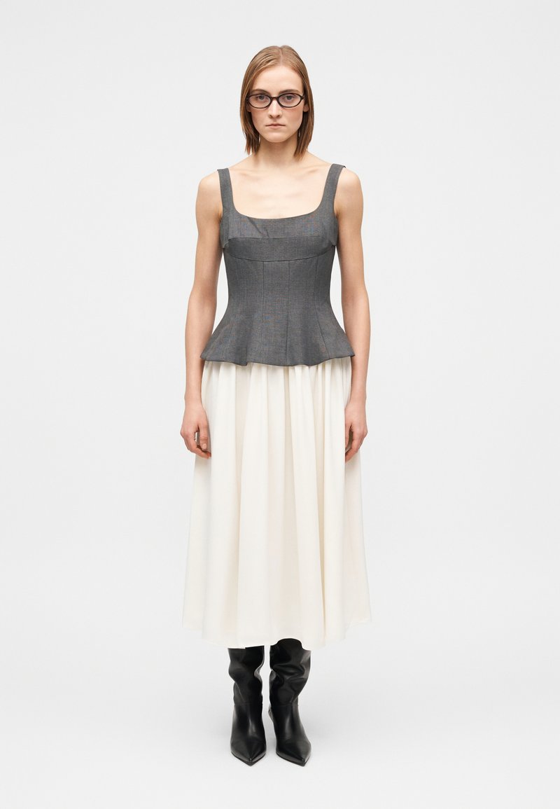 Γκρι peplum τοπ με ευρείες τιράντες, συνδυασμένο με  μια αέρινη κρεμ φούστα και μαύρες μπότες μέχρι το γόνατο. Η υφή είναι ομαλή με δομημένα σχεδιαστικά στοιχεία.