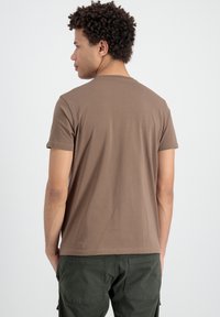 Camiseta de manga corta marrón hecha de algodón, con cuello redondo y un ajuste relajado, combinada con pantalones cargo verdes.