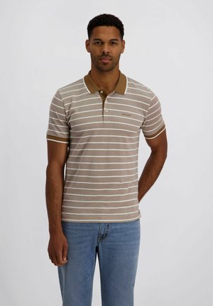 Mann trägt beige-weiß gestreiftes Poloshirt mit braunem Kragen und blauer Jeans, steht vor hellem einfarbigem Hintergrund.