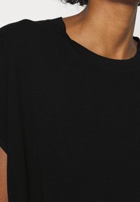 Černý pletený top s kulatým výstřihem a krátkými rukávy. Látka vypadá měkce a má mírně texturovaný vzhled, nabízí standardní střih.