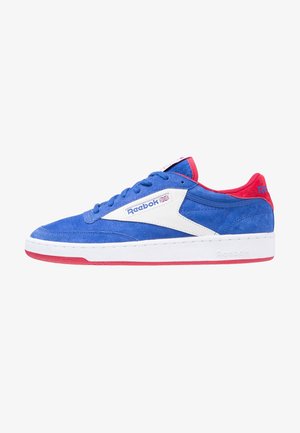 Baskets Reebok en daim bleu avec panneau latéral blanc, accents rouges au talon et à la semelle, et logo du drapeau britannique près des lacets.