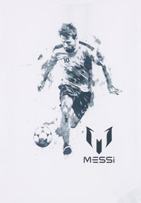 Λευκό μπλουζάκι με γραφικό σε μαύρο και γκρι ενός ποδοσφαιριστή σε κίνηση, με τον αριθμό 10 και το λογότυπο "MESSi" από κάτω.