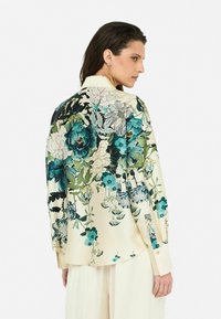 Seidene Bluse mit floralen Druck, die kräftige grüne und blaue Blumen auf einem cremefarbenen Hintergrund zeigt, mit langen Ärmeln und lässiger Passform.