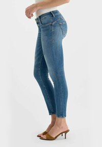 Strakke blauwe spijkerbroek gemaakt van denim, met een taille op het midden, vijf zakken en subtiele stiksel details. Draagt bruine sandalen met hak.