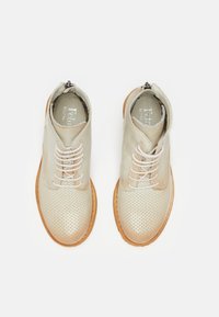 Zapatos de cuero perforado en color beige con punta redonda, cordones blancos y suela de goma en tono marrón. Cuenta con un cierre de cremallera en la parte posterior.