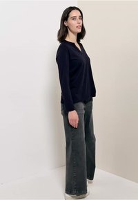 Navyblaues Langarmshirt mit V-Ausschnitt und seitlichen Schlitzen, kombiniert mit hochgeschnittenen, weit geschnittenen grauen Jeans und cremefarbenen Sneakers.