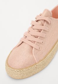 Baskets en toile rose avec un design à lacets, dessus texturé et semelle plateforme en jute tissée, mettant en avant le contraste entre les matériaux.