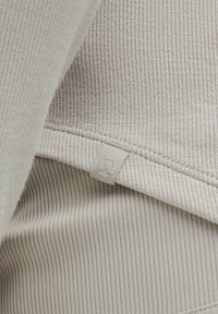 Lichtbeige ribbelstof met een gestructureerde oppervlakte; inclusief een zichtbaar label met een gestileerd embleem. Zachte en flexibele ontwerpe.