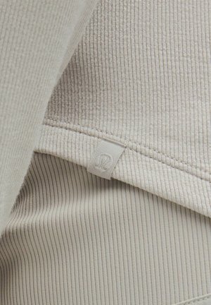 Lichtbeige ribbelstof met een gestructureerde oppervlakte; inclusief een zichtbaar label met een gestileerd embleem. Zachte en flexibele ontwerpe.