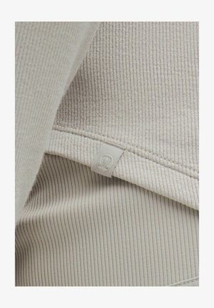 Lichtbeige ribbelstof met een gestructureerde oppervlakte; inclusief een zichtbaar label met een gestileerd embleem. Zachte en flexibele ontwerpe.