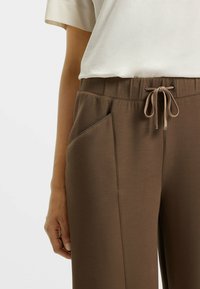 Bruine sweatpants van zachte stof, met een elastische tailleband met een trekkoord en zijzakken met contrasterende stikdetails.