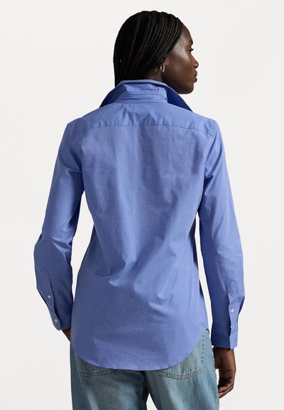 Chemise à manches longues bleue en coton uni, dotée d'un col classique, d'un empiècement au dos et de poignets boutonnés. Texture subtile avec une coupe décontractée.
