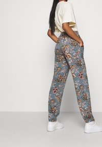 Kukkaprintti shortsit sinisestä kankaasta, joissa on monivärisiä kukkakuoseja. Varustettu sivutaskuilla ja joustavuuslahkeilla. Yhdistetty vaaleanväriseen t-paitaan.