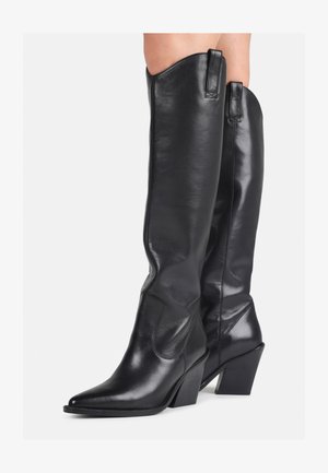 Cizme negre din piele, până la genunchi, cu vârf ascuțit, ioni curbat și toc masiv. Au o textură netedă și bucle pentru a fi trase pe sus.