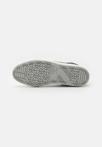 Šedá gumová podrážka tenisky s texturovaným, vzorovaným dnem. Mezi prvky patří bílá mezipodešev a jemný branding.