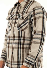 Beige flanellskjorta med brunt och blått rutmönster, med knäppta bröstfickor och krage. Mjuk textur, långa ärmar.